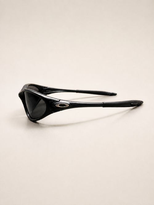 Rear three-quarter view of black Oakley Minute sunglasses, showing open temple arms and silver oval side details.