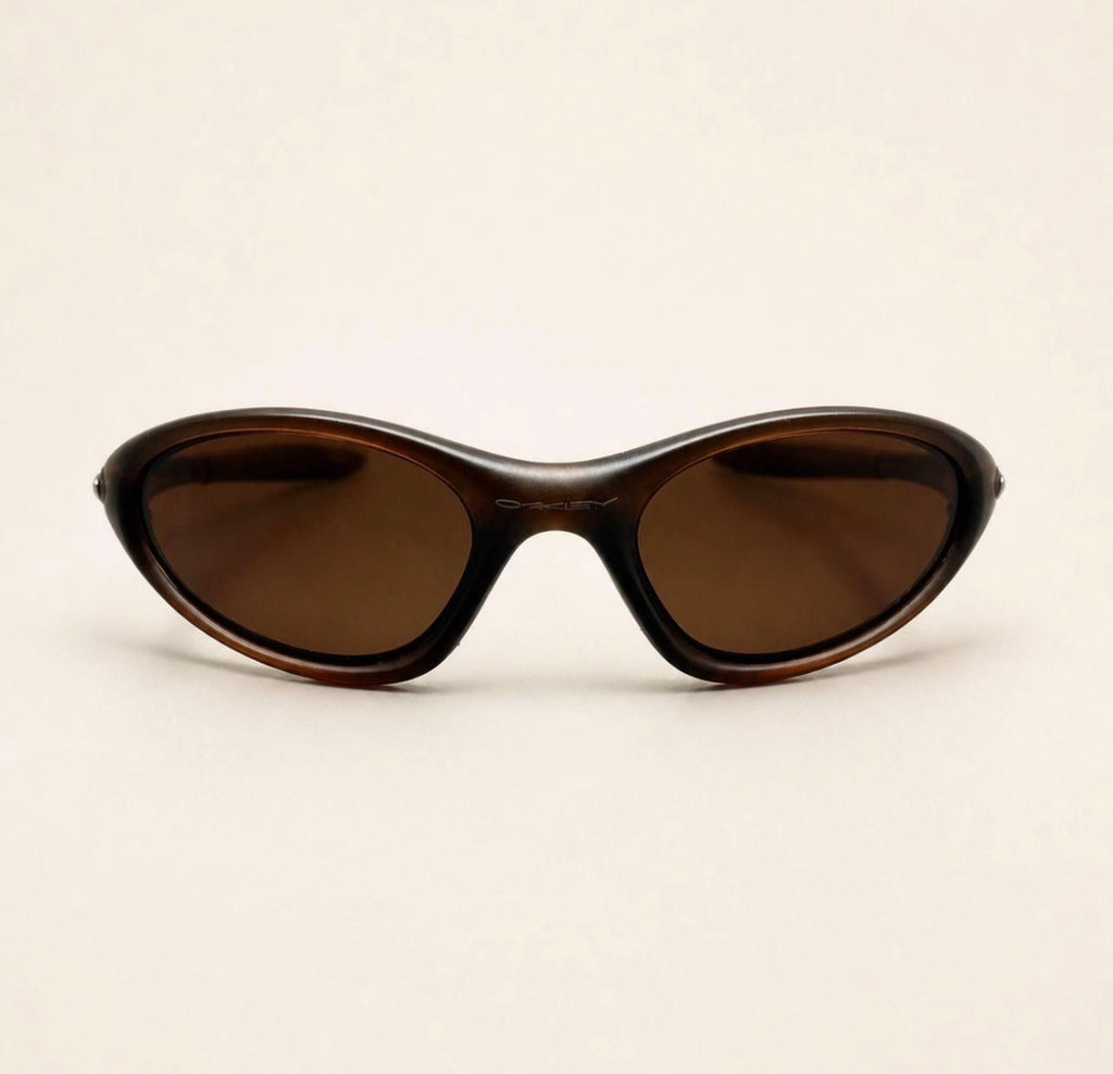 Front view of brown Oakley Minute sunglasses with warm brown lenses and a curved wraparound frame.