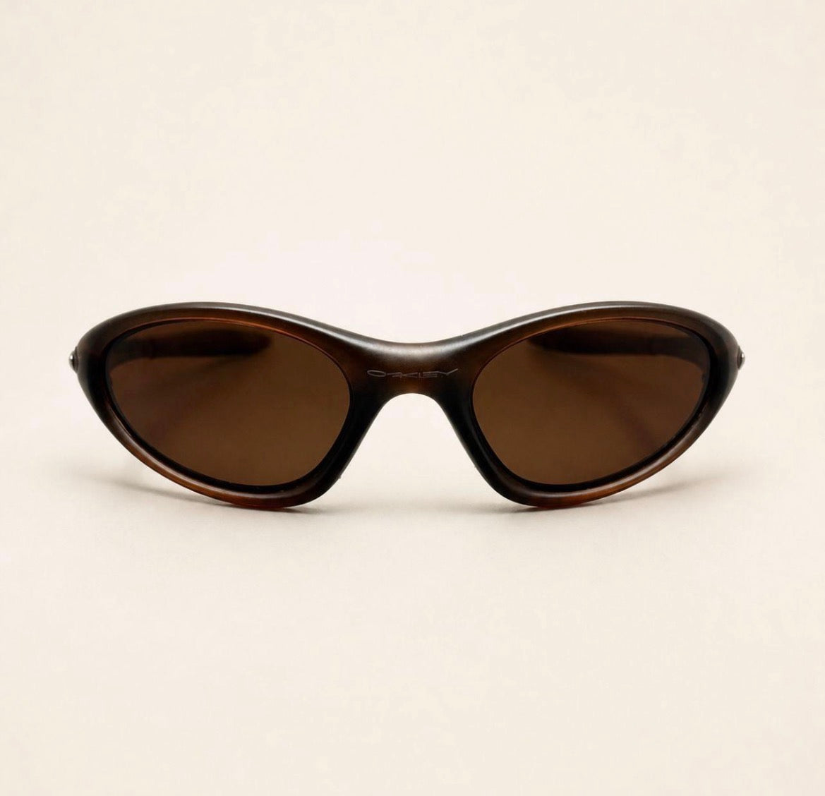 Front view of brown Oakley Minute sunglasses with warm brown lenses and a curved wraparound frame.